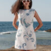 Nana Gotti white floral lace mini dress with blue embroidered detailing, sleeveless design, structured shoulders, and a flattering A-line silhouette, modeled by the seaside.