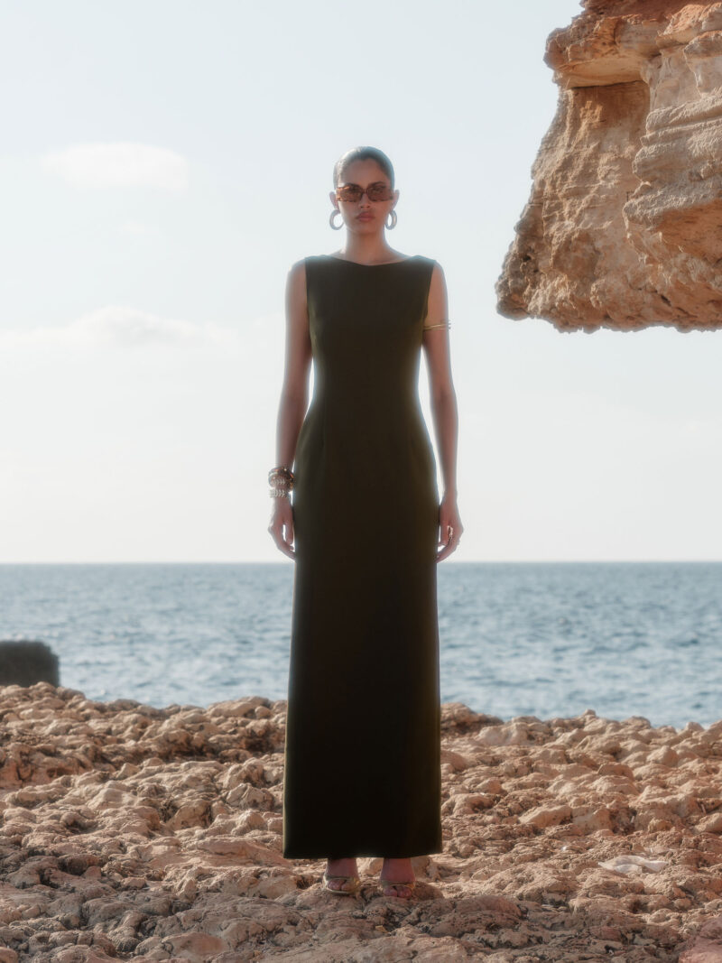 Lara olive green crepe maxi dress by Nana Gotti, featuring a sleeveless fitted silhouette and round neckline, photographed by the sea.