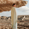 Model wearing the Nana Gotti Nerina Mint Green Fringe Cape Maxi Dress with cascading chiffon cape and fringe detailing, styled for luxury occasionwear against a natural rocky backdrop.
