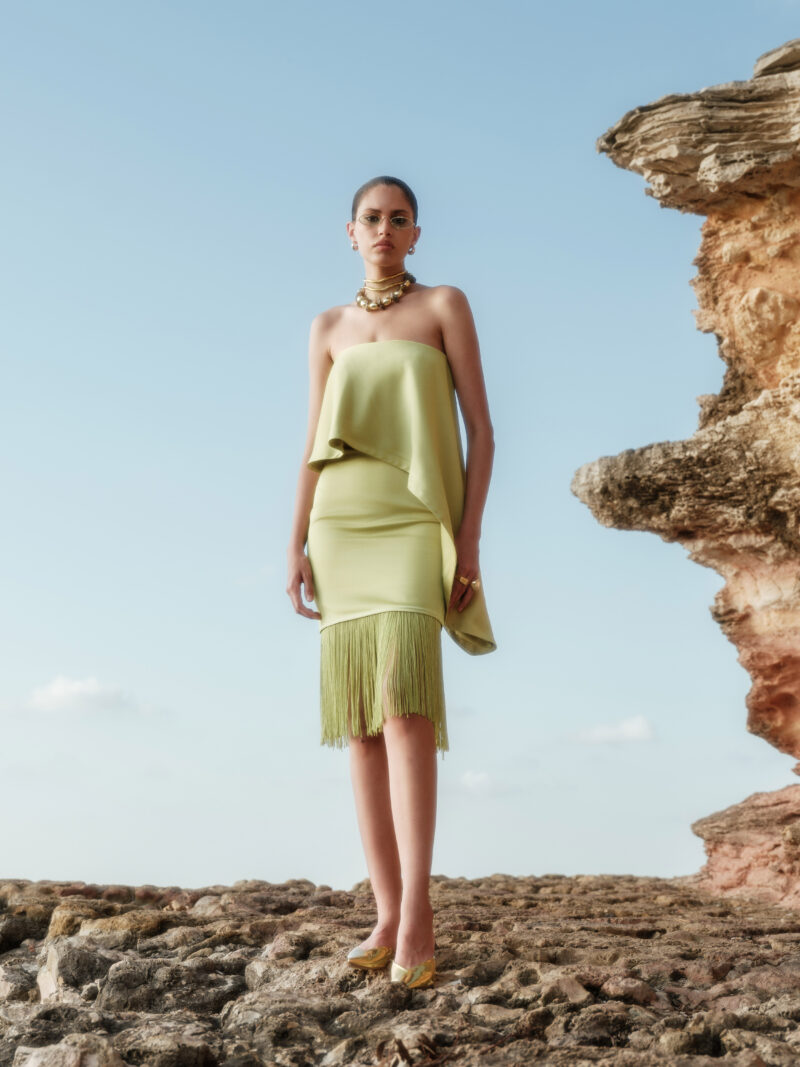 Riva Olive Green Crepe-Back Satin Fringe Midi Dress by Nana Gotti featuring a strapless neckline, asymmetric draped overlay, and long fringe hem, front view.