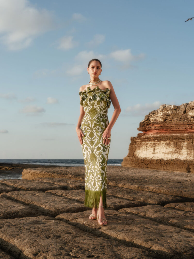 Nana Gotti Aelia olive-green botanical print maxi dress with strapless ruffles, fitted silhouette, and fringe hem by the sea.