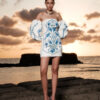 Model wearing the Nana Gotti Lalezar ivory crepe mini dress with blue floral print, strapless neckline and dramatic balloon sleeves at sunset by the sea.